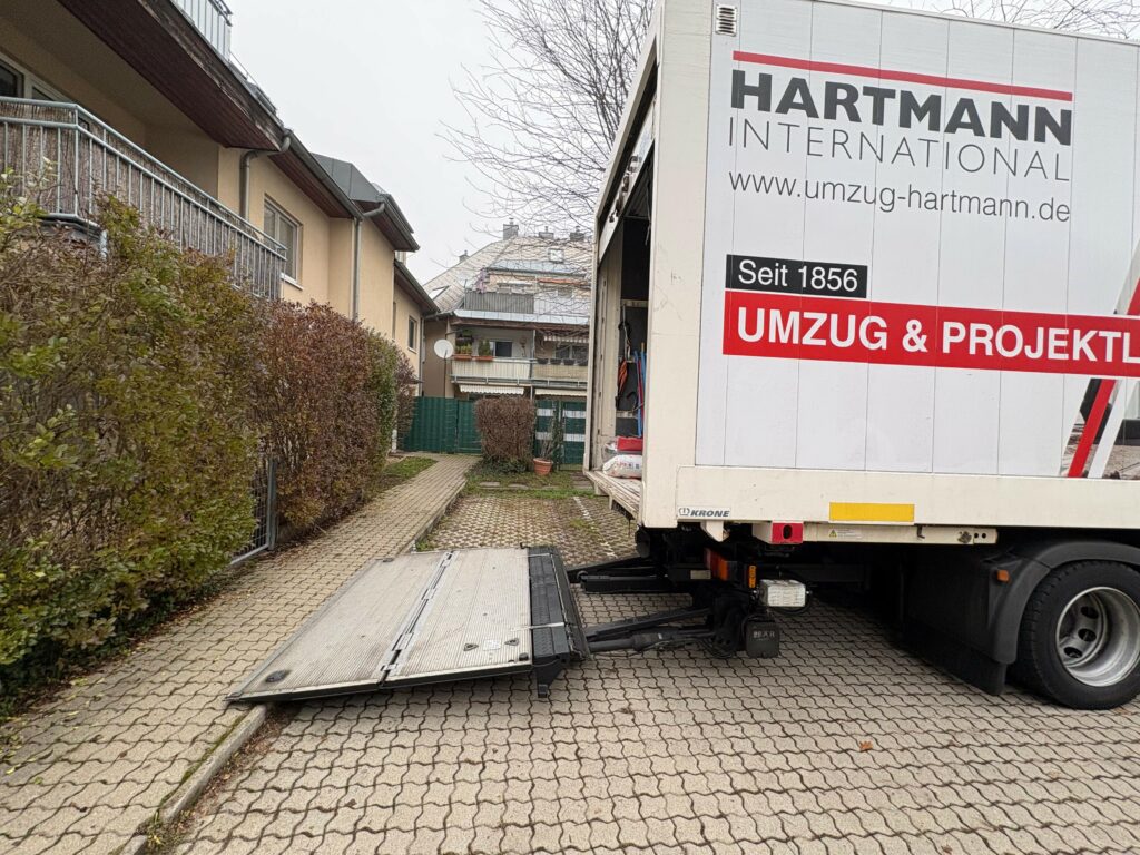 Privatumzug von Österreich nach Deutschland: Umzugstransporter von Hartmann International, mit offener Laderampe, vor Wohnhaus in Wien.